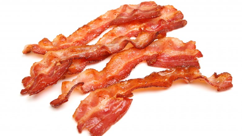 Bacon frying in stove top pan. Sizzling bacon strips in silver skillet.  Stock Photo