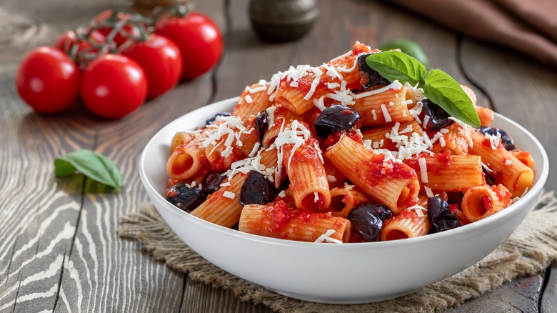 Pasta in a bowl with tomatoes in the background.