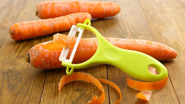 Carrots with a peeler on a wooden table