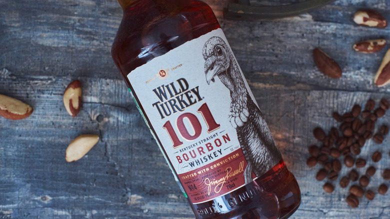 Bottle of Wild Turkey 101 laying on table with variety of nuts