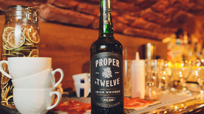 Bottle of Proper no. Twelve on bar with mugs and glasses