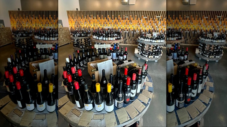 Four round wooden tables and a wall in the background all covered in assorted wine bottles from Crush Wine Bistro