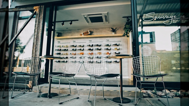 Two small patio tables with chairs outside Sauvage Bottle shop with rows of wine bottles on wall in shop background