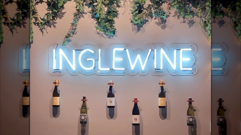Inglewine neon sign inside 1010 Wine and Events on wall below decorative ivy and above wine bottles fasted on wall