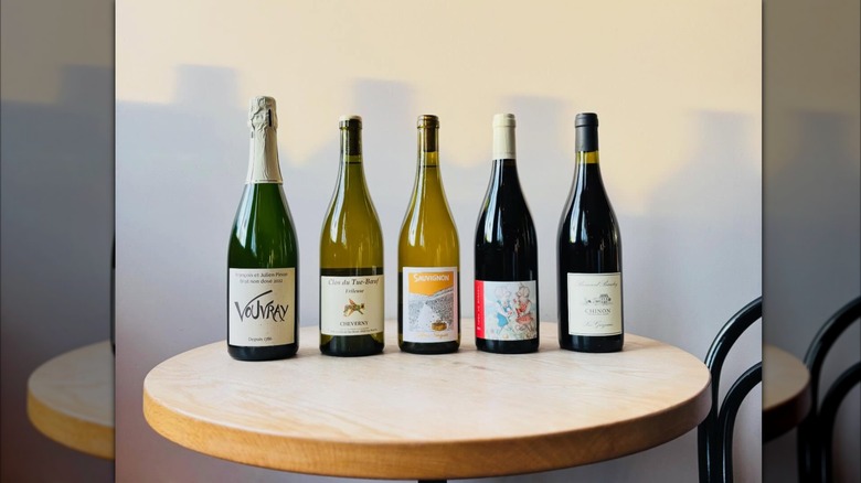 5 bottles of wine on a table at Maine & Loire. In order, Vouvray, Chevery, Sauvignon, a bottle with a red label and 2 dogs playing together, and a bottle of Chinon.