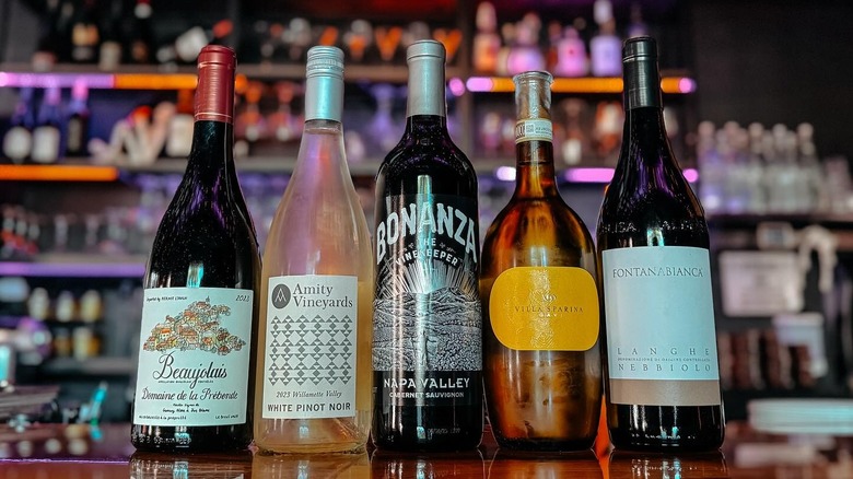 5 bottles of wine. From left to right: Beaujolais, Amity Vineyards white Pinot Noir, Bonanza cabernet sauvignon, villa sparina Gavi, and a Fontana Bianca Lange Nebbiolo