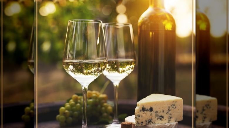 2 glasses and a bottle of wine, a piece of blue cheese and some green grapes.