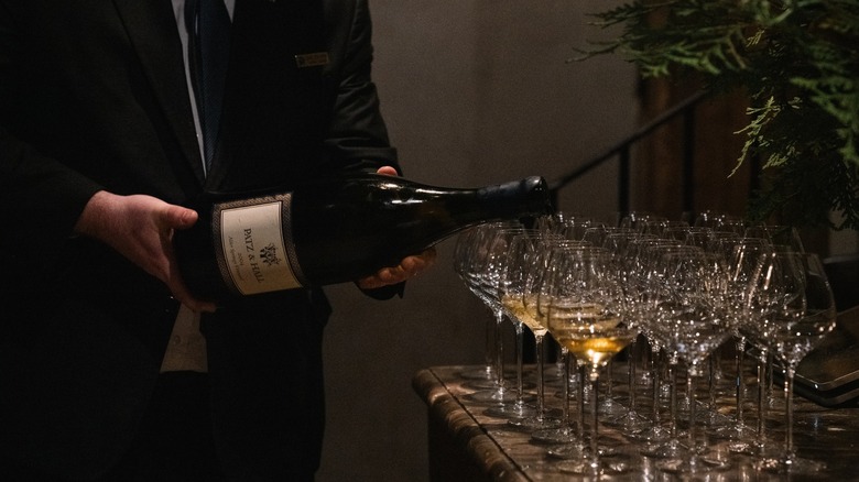 A person holding a bottle of wine and filling up several glasses.