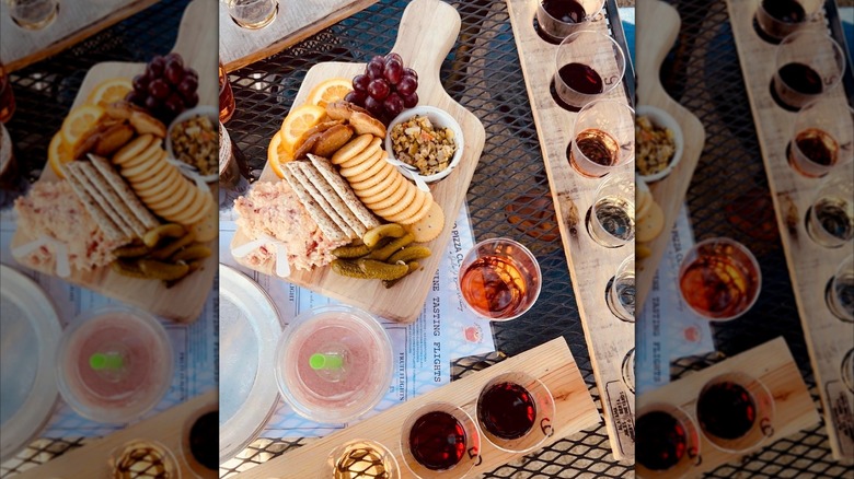 An overhead view of a wine tasting setup with wooden flight boards of red, white, and rosé wines, plus a charcuterie board with crackers, cheese spread, pickles, grapes, and orange slices