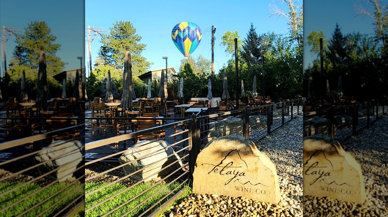 An outdoor patio at Telaya Wine Co. with tables and umbrellas, a stone winery sign, and a hot air balloon floating above