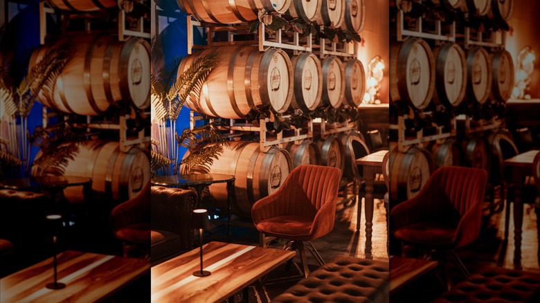 Warmly-lit winery interior with stacked oak barrels and velvet seating
