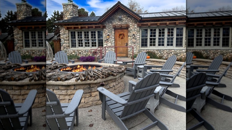 A blazing fire pit surrounded by Adirondack chairs in front of a stone building with a glass of red wine on one of the Adirondack chairs
