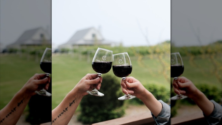 Two hands clinking glasses of red wine with the Carlos Creek Winery label on the wine glasses