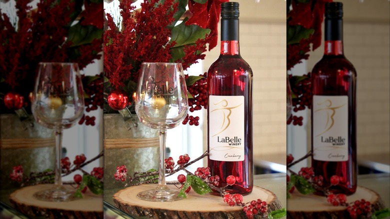 A bottle of cranberry wine from LaBelle Winery next to an empty wine glass with frosted cranberries as decoration