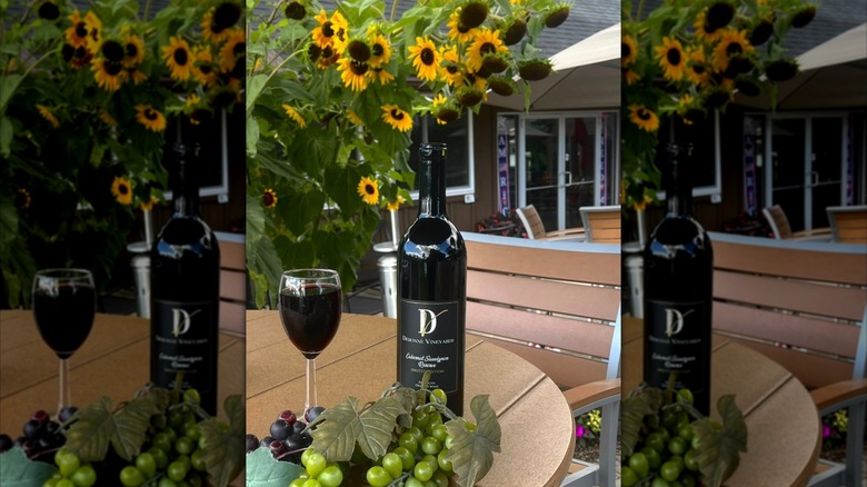 Bottle of Debonné Vineyards Cabernet Sauvignon next to a full  glass with grapes and sunflowers as decoration