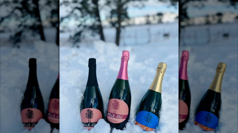 Three bottles of sparkling wine with Belle Joli Winery labels in the snow