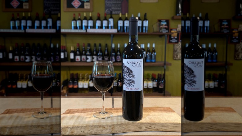 A glass of red wine next to a bottle of Chestnut Ridge Winery's Nebbiolo on a wooden table