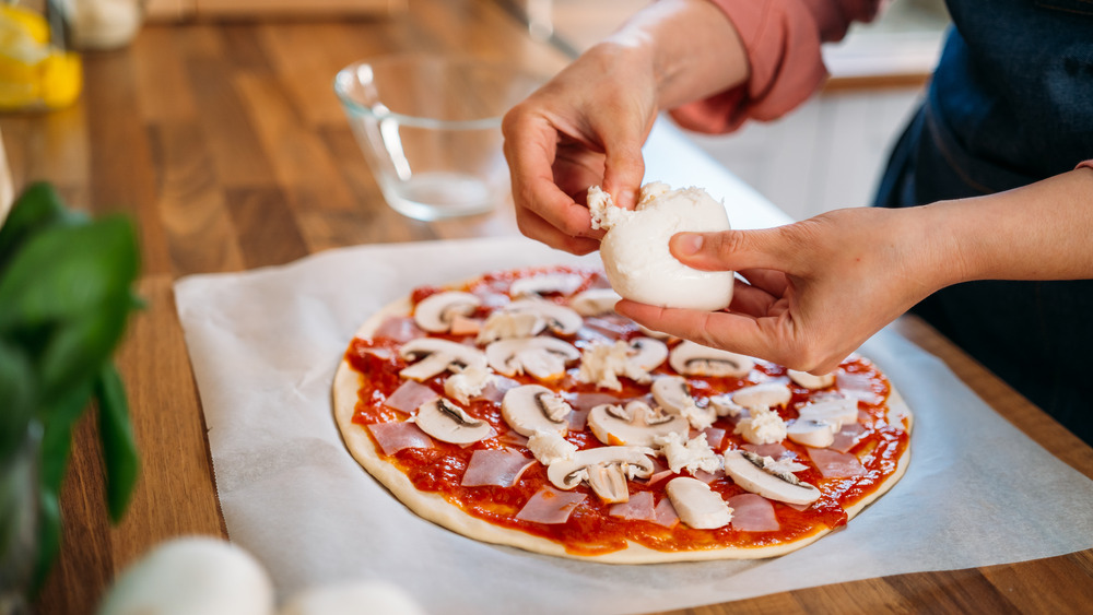 Person adding cheese to pizza