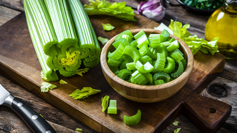 Bowl of chopped celery beside stalk on cutting board