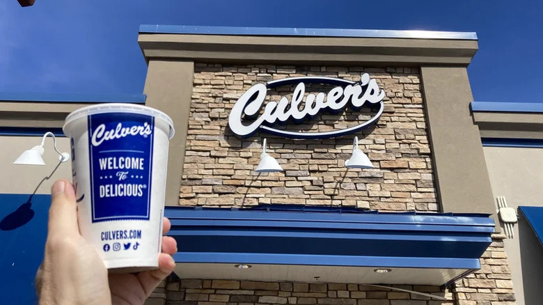 Hand holding a Culver's Coke cup in front of a branch of Culver's