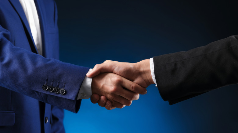 The arms of two people wearing suits shaking hands