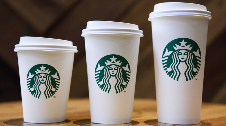 Three sizes of Starbucks paper coffee cups sit on a wooden table.