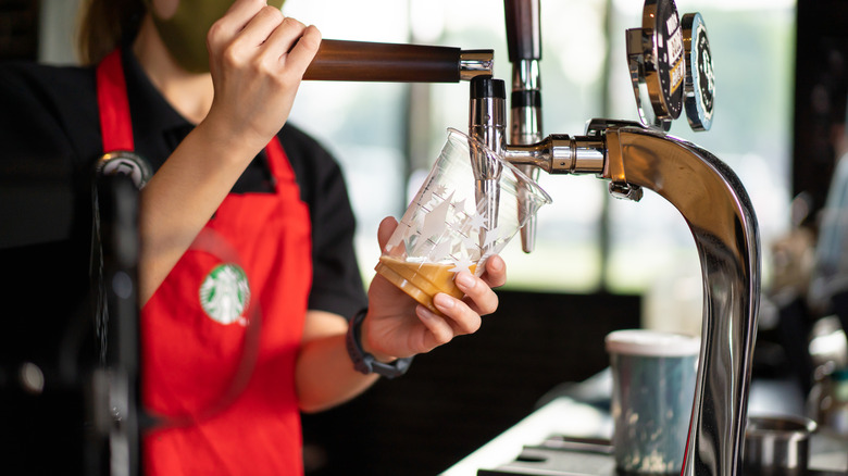Starbucks employee fills plastic takeout cup from nitro cold brew tap.