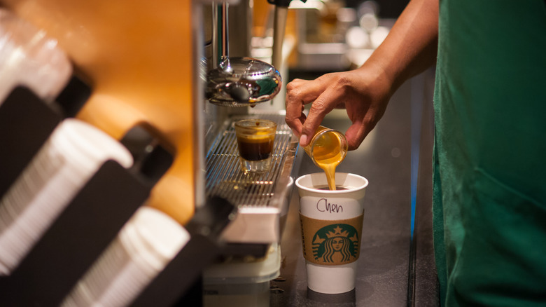 Starbucks barista pours a shot of espresso into a takeout cup.