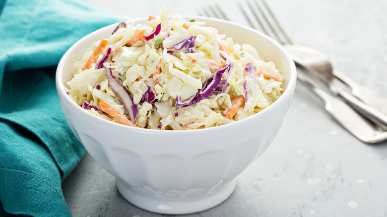 Small bowl of coleslaw on table with utensils and napkin
