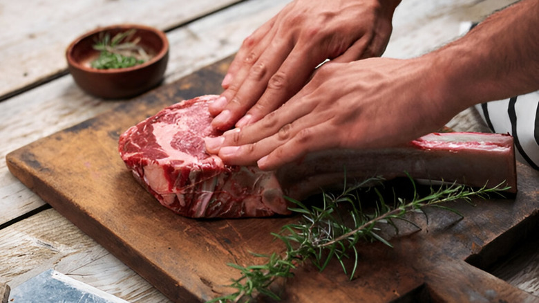 Hands patting seasoning onto steak