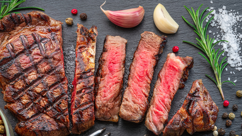 Sliced ribeye with seasonings and herbs on black background