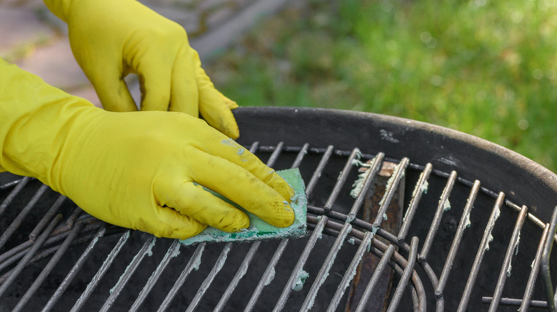 Yellow gloved hands cleaning grill grates with a green sponge