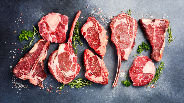 Cuts of raw meat with salt and fresh herbs on black background