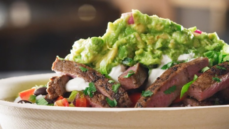 A brown cardboard bowl filled with carne asada and green guacamole