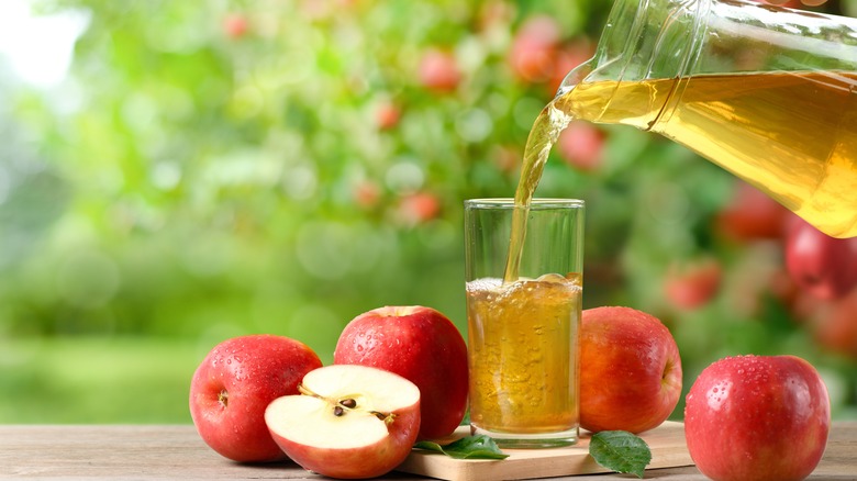 Apple juice poured into a glass with apples on side