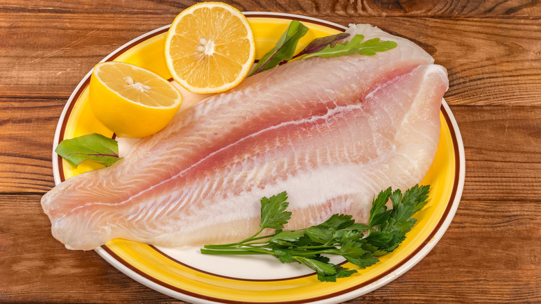 A defrosted basa fillet with lemon halves on a plate