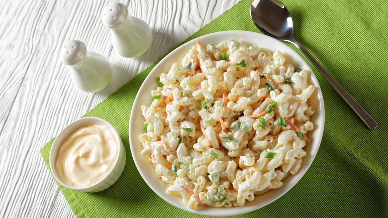 Bowl of macaroni salad with spoon, salt and pepper shakers, and side of mayonnaise