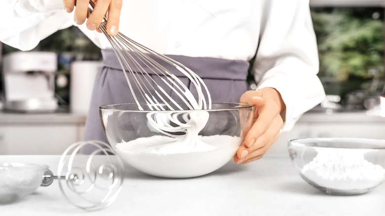 Hands whisking whipped cream in glass bowl