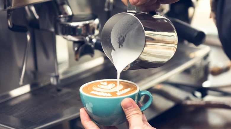 Person pouring milk from a steel jug into a coffee cup