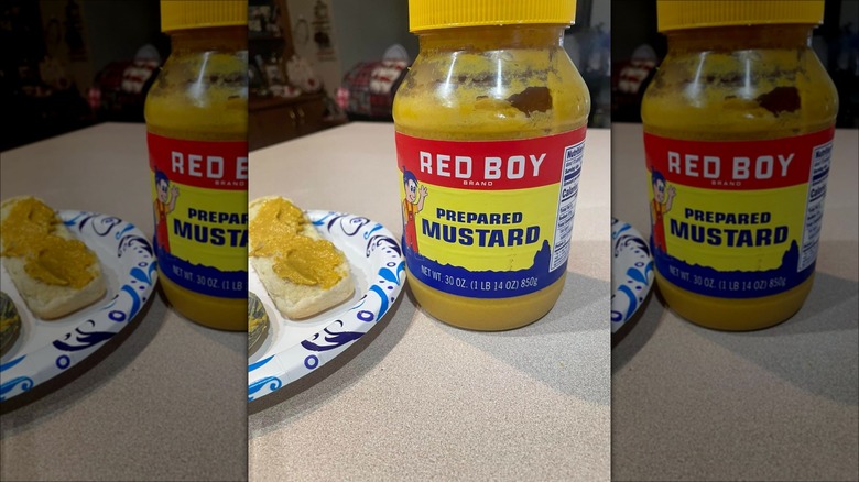 Jar of Red Boy brand mustard next to sandwich on paper plate