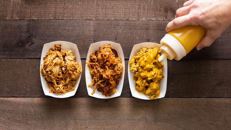 Squeezing bottle of Carolina-style mustard barbecue sauce onto pulled pork