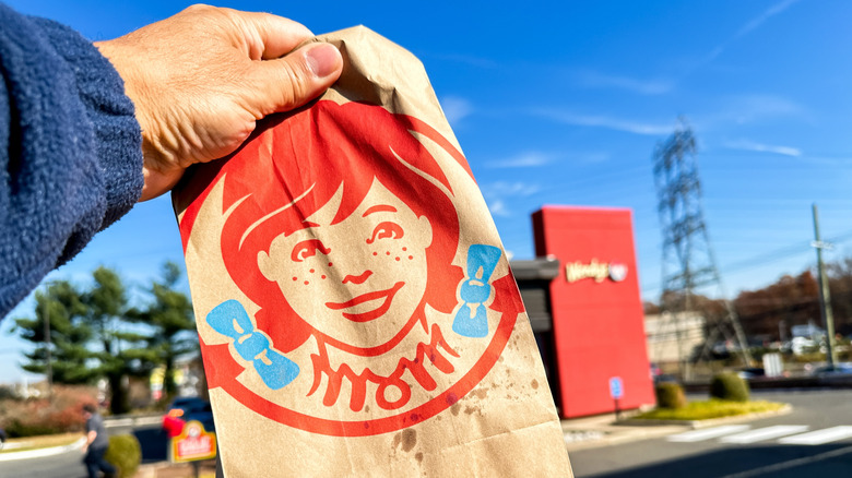 Hand holding Wendy's takeout bag in front of restaurant