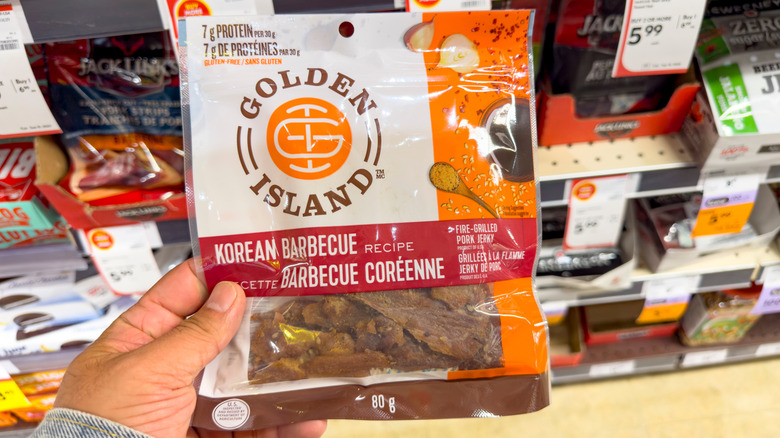 A hand holding a pack of Golden Island Korean BBQ Pork Jerky at a grocery aisle