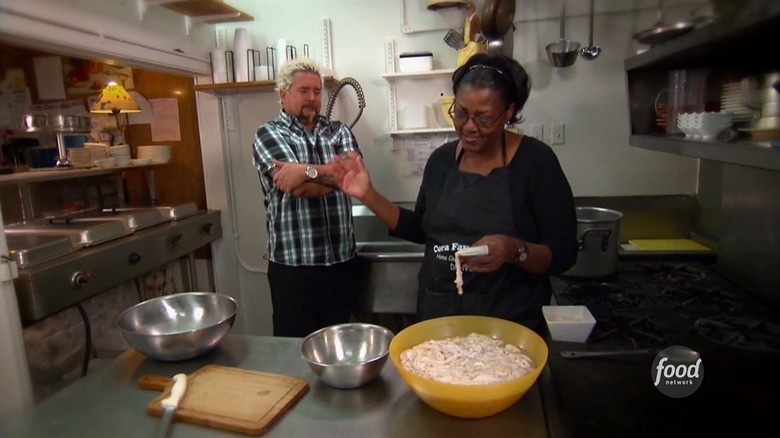 Guy Fieri looks anxious with both arms folded as Cora Faye from Cora Faye's Cafe washes large pig intestines for chitterlins
