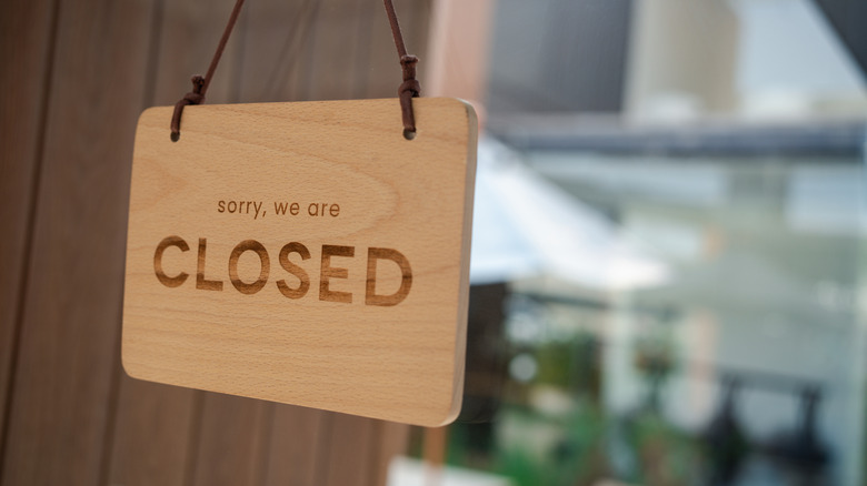 A wooden "CLOSED" sign hangs against the clear glass of a shop