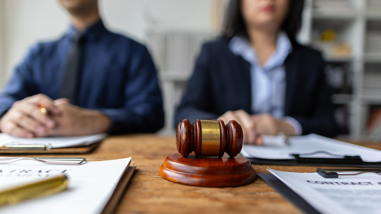 A man and a woman sits behind a desk, documents and a gavel on the table before them