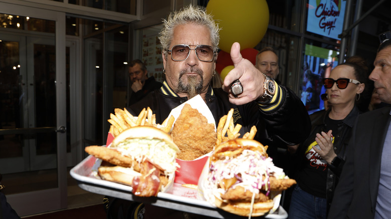 Guy Fieri holding a tray of burgers, fries chicken, and fries