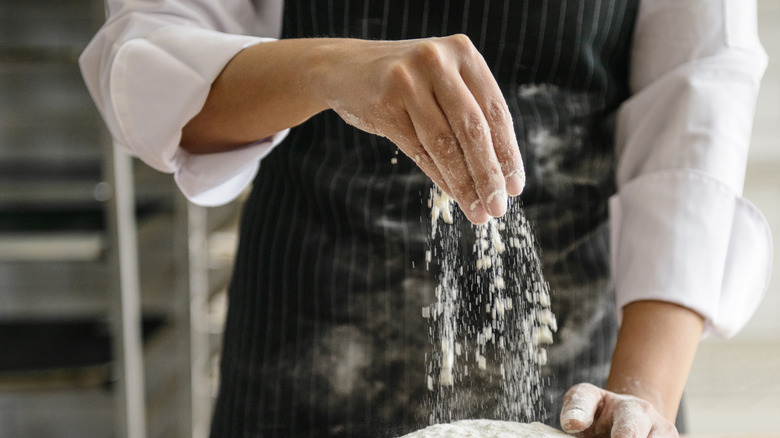 Hands of a chef sprinkling flour on a dough with sleeves rolled up