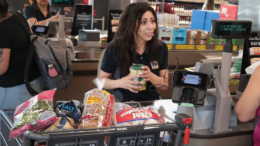 An Aldi cashier at her cash register next to a full cart.