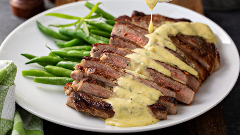 bearnaise sauce being poured on a sliced steak on a white plate